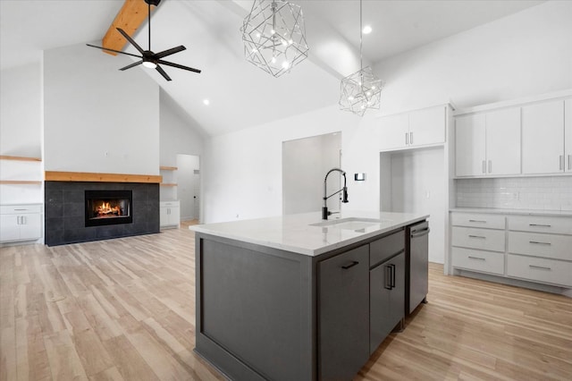 kitchen with high vaulted ceiling, decorative light fixtures, white cabinetry, a kitchen island with sink, and stainless steel dishwasher