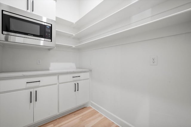 kitchen with stainless steel microwave, white cabinetry, and light hardwood / wood-style floors