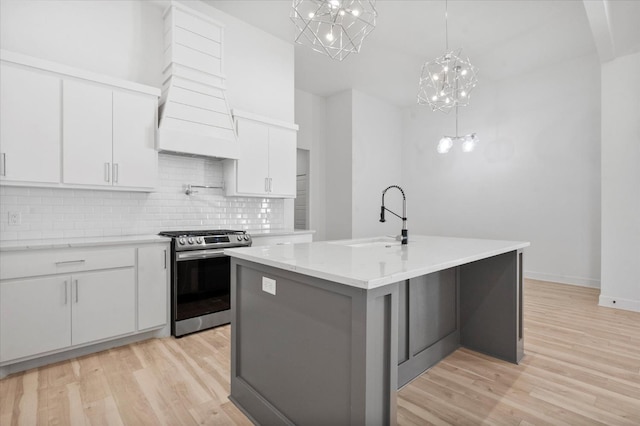 kitchen with sink, stainless steel range with gas stovetop, white cabinets, and a center island with sink