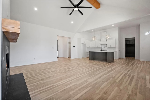 unfurnished living room with sink, ceiling fan, beam ceiling, high vaulted ceiling, and light hardwood / wood-style floors