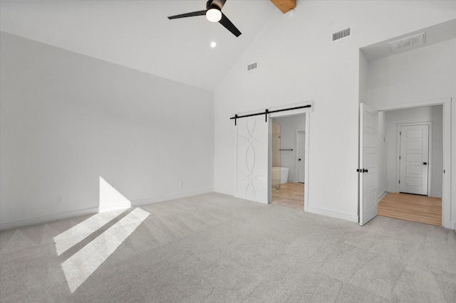 unfurnished bedroom with high vaulted ceiling, beamed ceiling, ceiling fan, a barn door, and ensuite bath