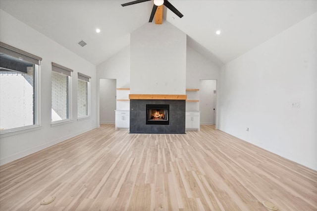 unfurnished living room with ceiling fan, high vaulted ceiling, light hardwood / wood-style floors, a tiled fireplace, and beamed ceiling