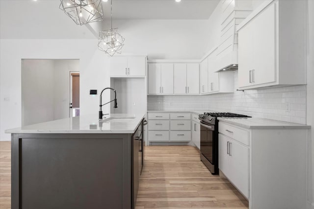 kitchen featuring sink, a kitchen island with sink, white cabinets, gas range, and decorative light fixtures