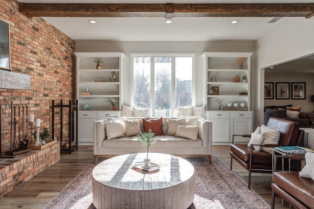 living room with beamed ceiling, wood-type flooring, a brick fireplace, and built in shelves