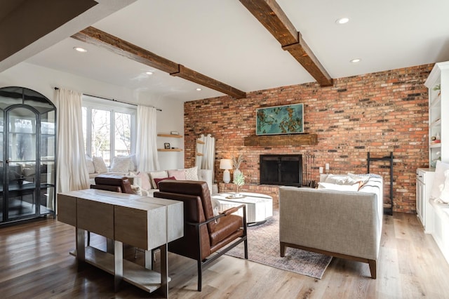 living room with a fireplace, beamed ceiling, brick wall, and light wood-type flooring