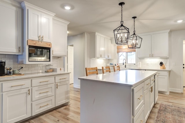 kitchen with sink, light hardwood / wood-style floors, white cabinets, a kitchen island, and decorative light fixtures