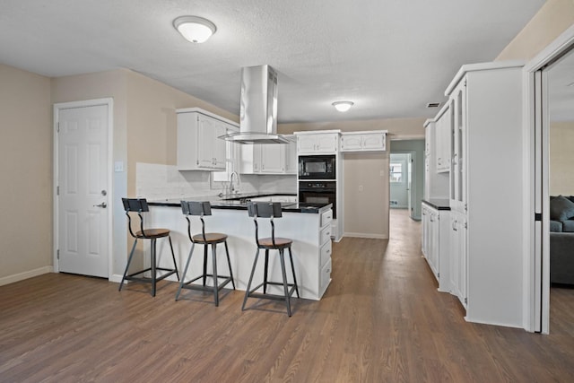 kitchen featuring island range hood, kitchen peninsula, white cabinetry, a kitchen bar, and black appliances