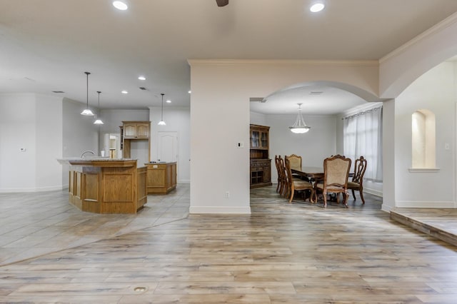 kitchen with pendant lighting, ornamental molding, ceiling fan, a center island with sink, and light hardwood / wood-style flooring