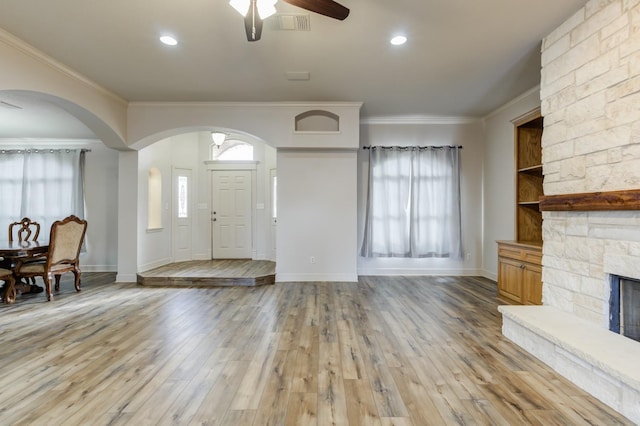 foyer with crown molding, a stone fireplace, light hardwood / wood-style floors, and ceiling fan