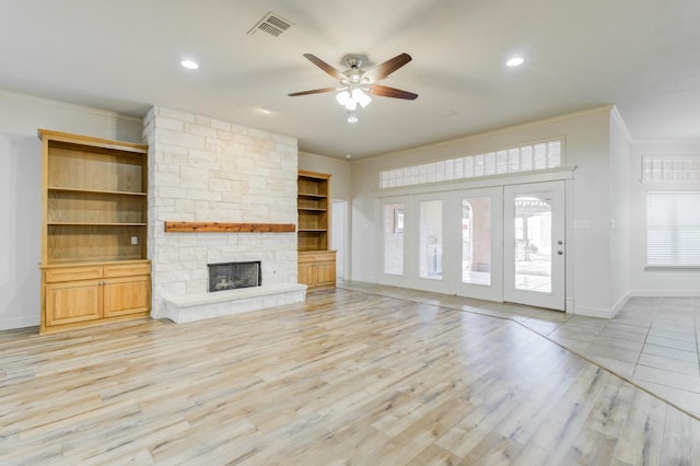 unfurnished living room featuring crown molding, a stone fireplace, ceiling fan, and light wood-type flooring