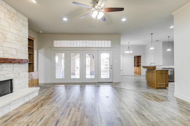 unfurnished living room with ceiling fan with notable chandelier, built in features, a fireplace, ornamental molding, and light wood-type flooring