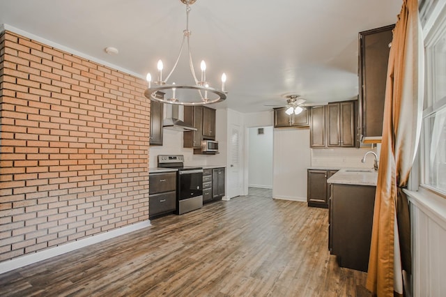 kitchen with brick wall, appliances with stainless steel finishes, ceiling fan with notable chandelier, sink, and dark hardwood / wood-style flooring