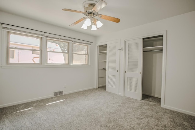 unfurnished bedroom with two closets, light carpet, and ceiling fan