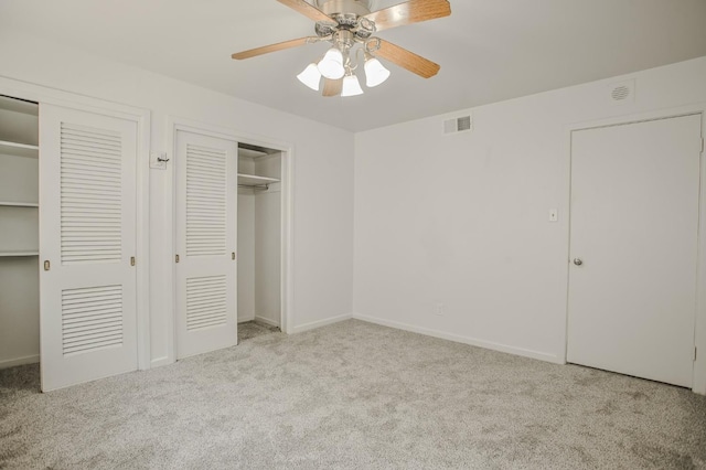 unfurnished bedroom featuring light carpet, ceiling fan, and multiple closets