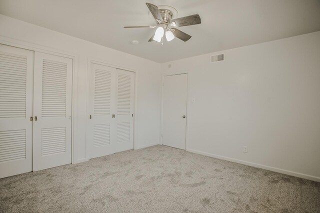 unfurnished bedroom with multiple closets, light carpet, and ceiling fan