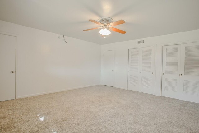 unfurnished bedroom with two closets, light colored carpet, and ceiling fan