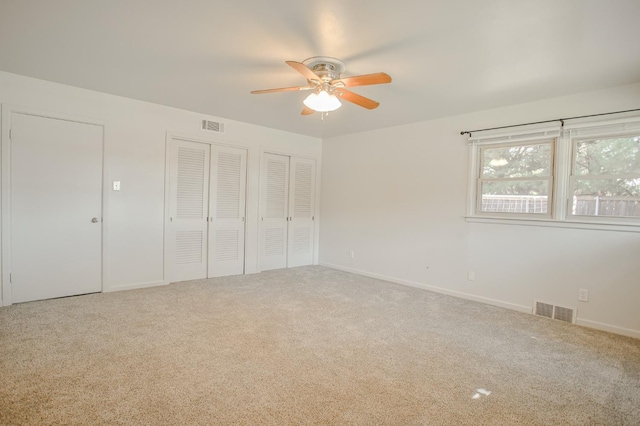 unfurnished bedroom featuring ceiling fan, carpet floors, and two closets