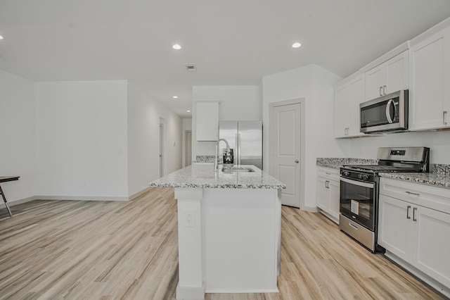 kitchen featuring light wood finished floors, light stone countertops, a center island with sink, white cabinetry, and appliances with stainless steel finishes