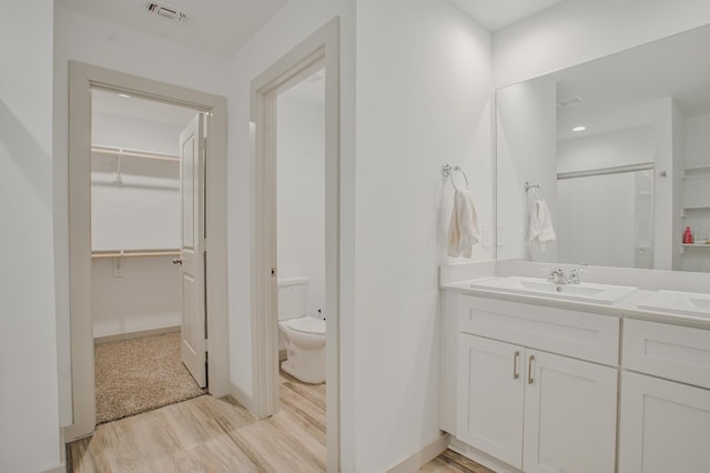 full bath featuring a spacious closet, wood finished floors, toilet, vanity, and visible vents