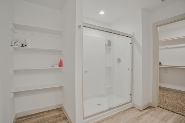 bathroom featuring baseboards, a spacious closet, wood finished floors, and a shower stall