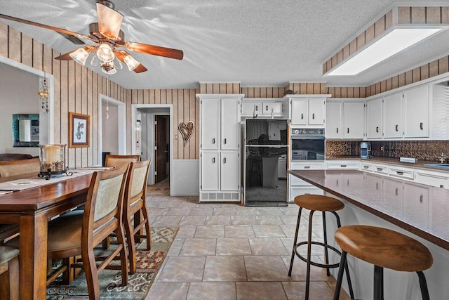 4405 56th St, Lubbock, TX 79414 - kitchen featuring oven, light stone finish floors, fridge, a ceiling fan, and white cabinetry