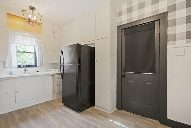 kitchen with sink, hanging light fixtures, light wood-type flooring, black refrigerator, and white cabinets