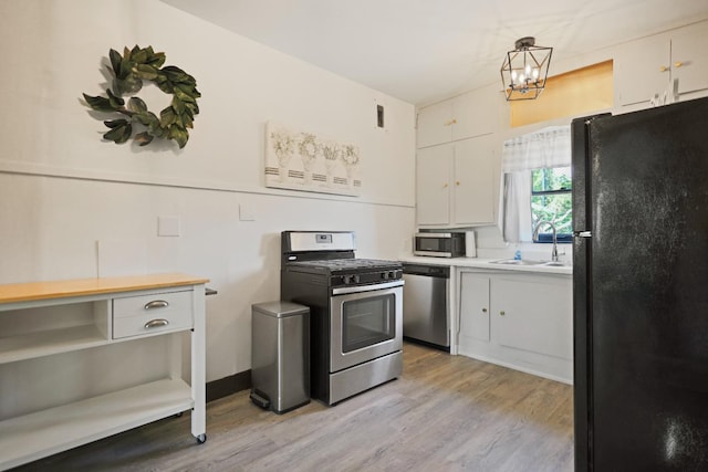 kitchen with decorative light fixtures, white cabinetry, sink, stainless steel appliances, and light hardwood / wood-style flooring