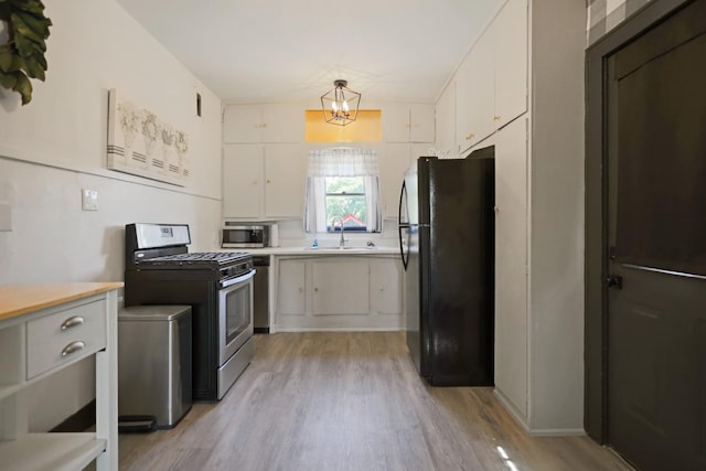 kitchen featuring sink, appliances with stainless steel finishes, white cabinetry, decorative light fixtures, and light wood-type flooring