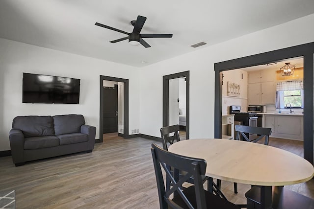 dining area with sink, ceiling fan with notable chandelier, and light hardwood / wood-style floors