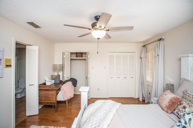 bedroom featuring hardwood / wood-style floors, ceiling fan, two closets, and a textured ceiling