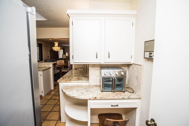 kitchen featuring light tile patterned flooring, white cabinetry, a textured ceiling, light stone countertops, and decorative backsplash