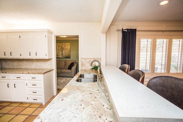 kitchen featuring light tile patterned flooring, a breakfast bar, sink, white cabinets, and decorative backsplash