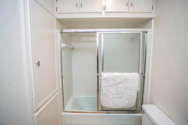 bathroom with bath / shower combo with glass door and toilet