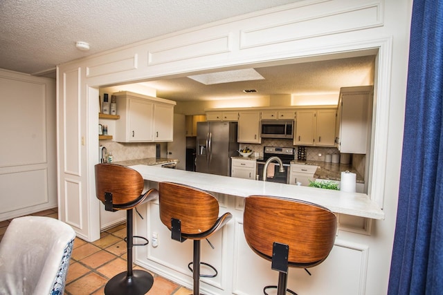 kitchen featuring a breakfast bar, appliances with stainless steel finishes, kitchen peninsula, and backsplash