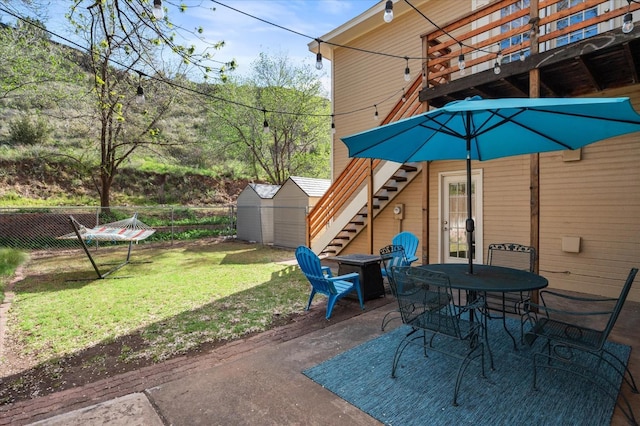 view of patio featuring an outdoor structure, fence, a shed, stairs, and outdoor dining space