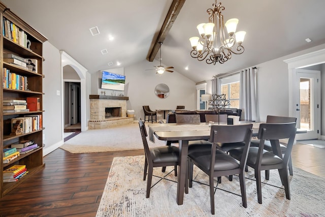 dining room featuring lofted ceiling with beams, a stone fireplace, hardwood / wood-style floors, and ceiling fan