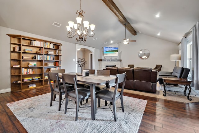 dining area with vaulted ceiling with beams, ceiling fan with notable chandelier, dark wood-type flooring, and a fireplace