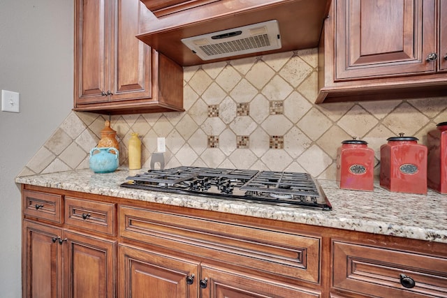 kitchen with ventilation hood, black gas stovetop, light stone countertops, and backsplash