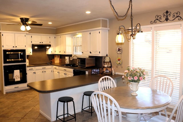 kitchen with white cabinets, dark countertops, under cabinet range hood, black appliances, and a sink