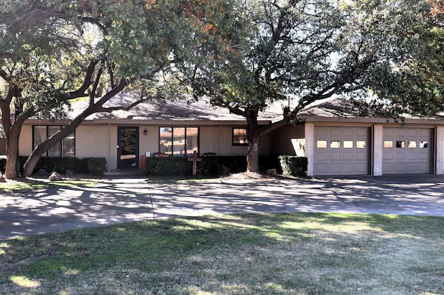 mid-century home with driveway, an attached garage, a front lawn, and brick siding