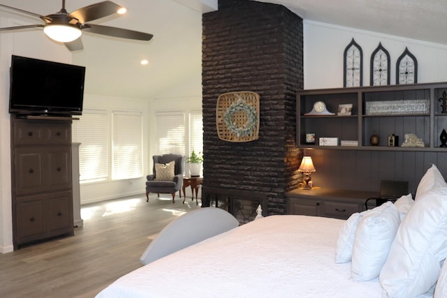 bedroom with vaulted ceiling, a fireplace, wood finished floors, and a ceiling fan