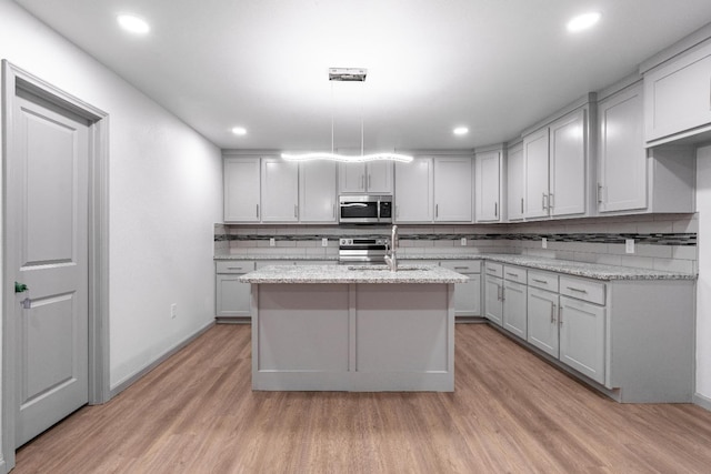 kitchen with stainless steel appliances, an island with sink, light stone countertops, and hanging light fixtures