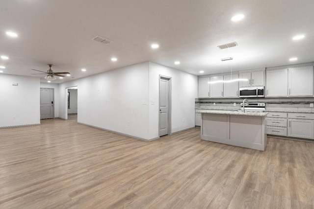 kitchen featuring white cabinetry, stainless steel appliances, decorative backsplash, an island with sink, and decorative light fixtures