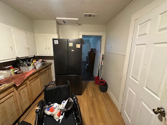 kitchen with white cabinetry, light hardwood / wood-style flooring, a textured ceiling, and black fridge