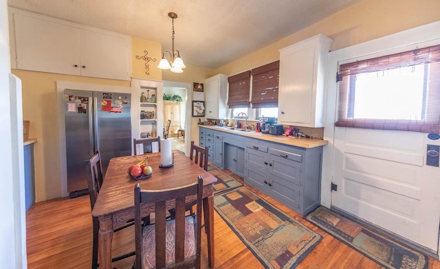 kitchen featuring sink, white cabinetry, a chandelier, hanging light fixtures, and stainless steel fridge