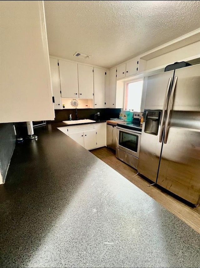 kitchen featuring stainless steel appliances, white cabinetry, sink, and a textured ceiling