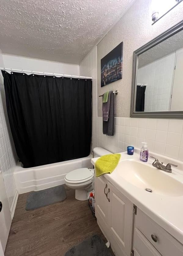 full bathroom with tile walls, hardwood / wood-style floors, vanity, a textured ceiling, and toilet