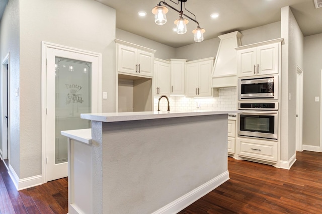 kitchen with appliances with stainless steel finishes, white cabinetry, tasteful backsplash, an island with sink, and decorative light fixtures