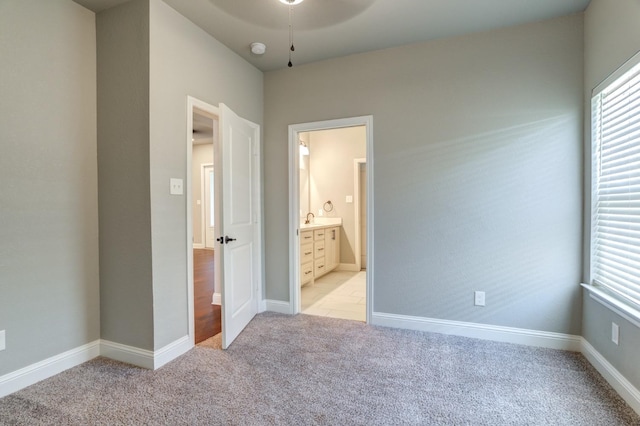 unfurnished bedroom with multiple windows, connected bathroom, light colored carpet, and sink