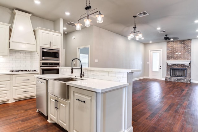 kitchen featuring appliances with stainless steel finishes, decorative light fixtures, white cabinetry, sink, and custom range hood